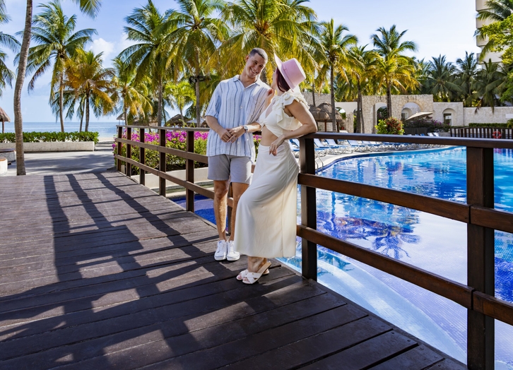 Couple on the wooden bridge over the pool overlooking the sea at Oasis Palm